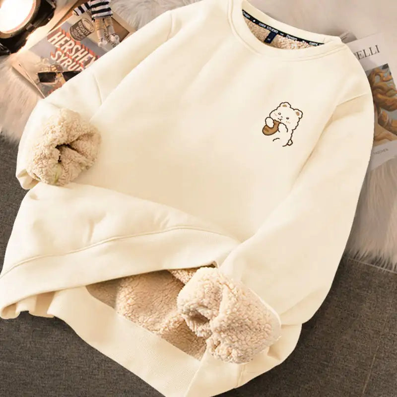 Close-up of a cream-colored women's sweater with a soft fleece lining and a small bear graphic on the chest.
