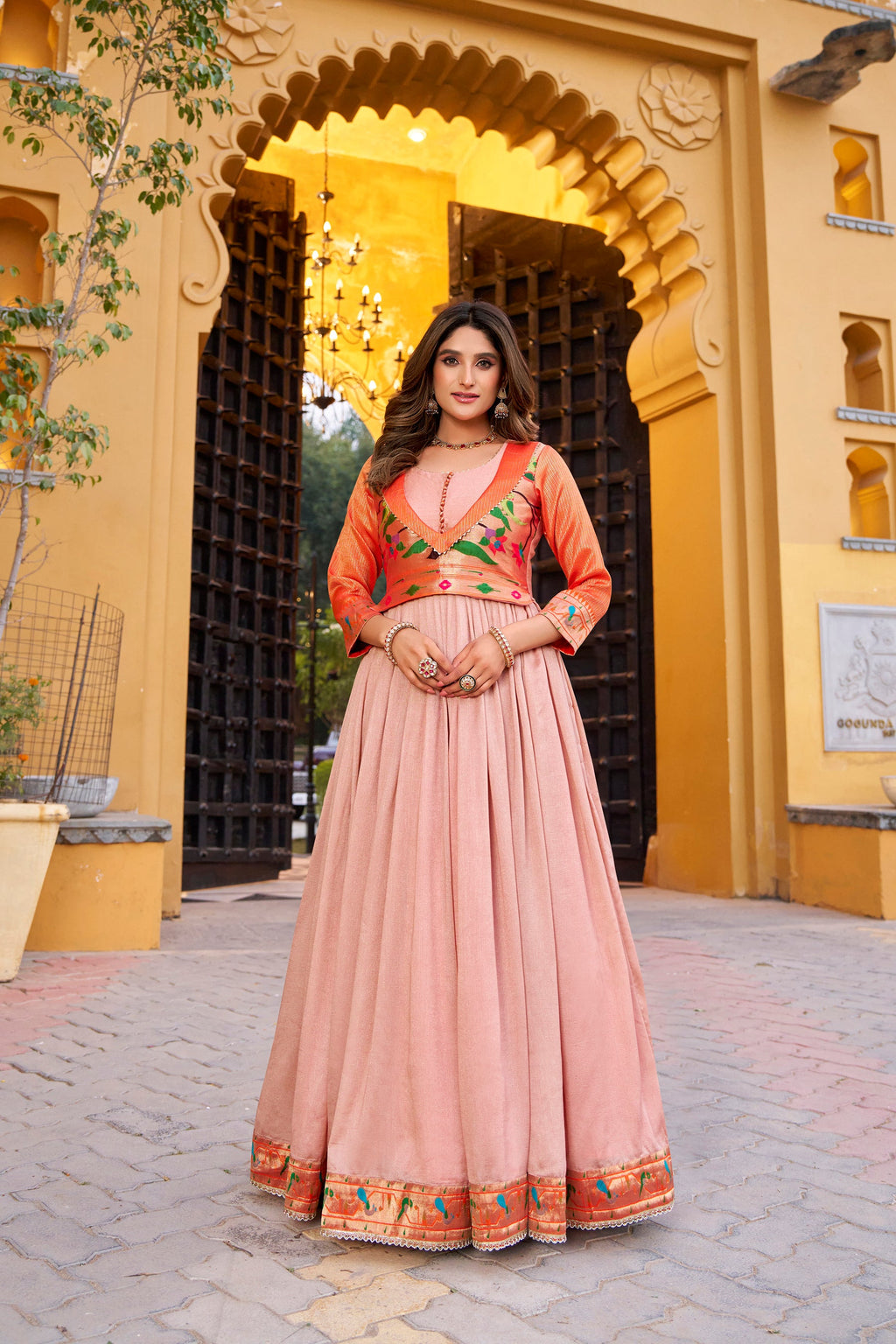A floor-length peach Vichitra silk dress with intricate gold Zari weaving and lace trim for a formal ethnic look.