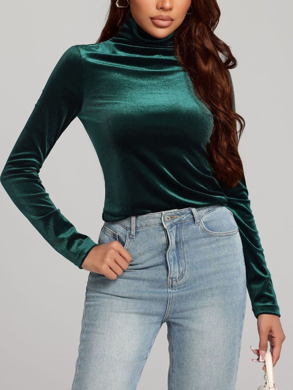 A woman wearing a long-sleeve emerald green turtleneck top made of a soft, slightly shimmering velvet-like fabric.
