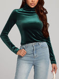 A woman wearing a long-sleeve emerald green turtleneck top made of a soft, slightly shimmering velvet-like fabric.