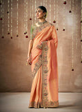 A vibrant orange organza silk designer saree with detailed embroidery.