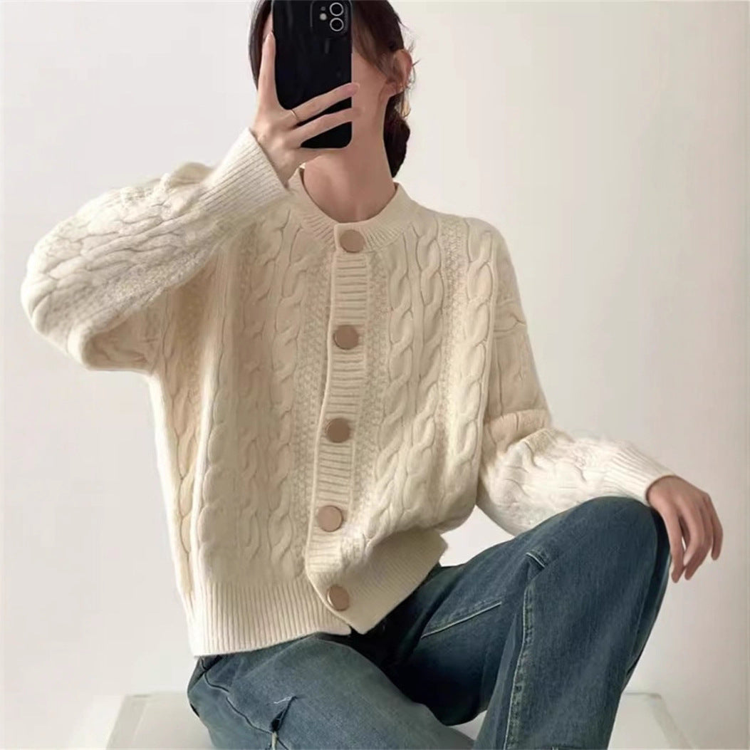 A woman wearing a gentle style cable knit cardigan with a round neck and button closure, in cream and light blue color options.