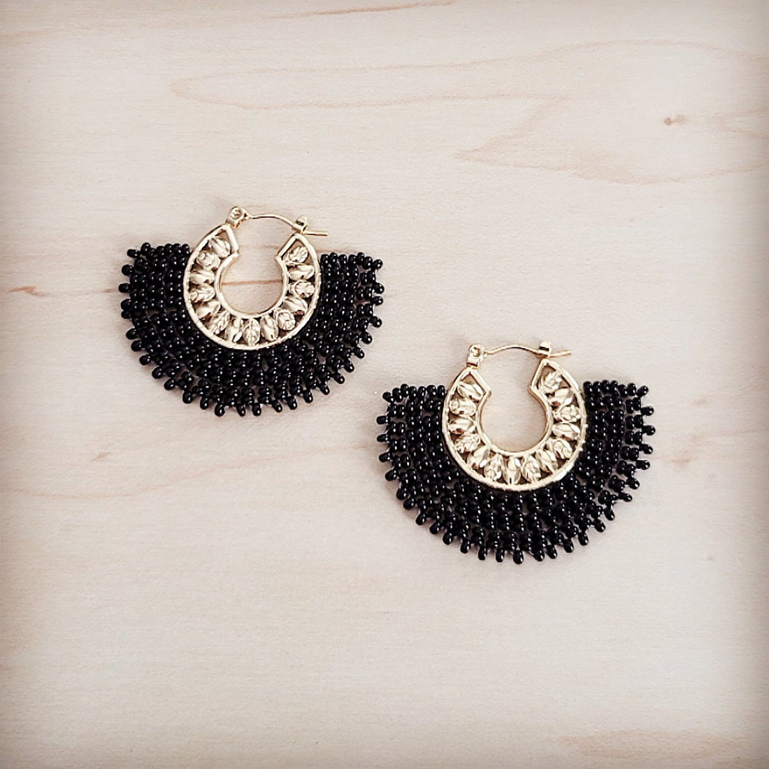 Pair of gold-tone hoop earrings with a semi-circular fan of black seed beads and small clear crystal accents on a light wood background.