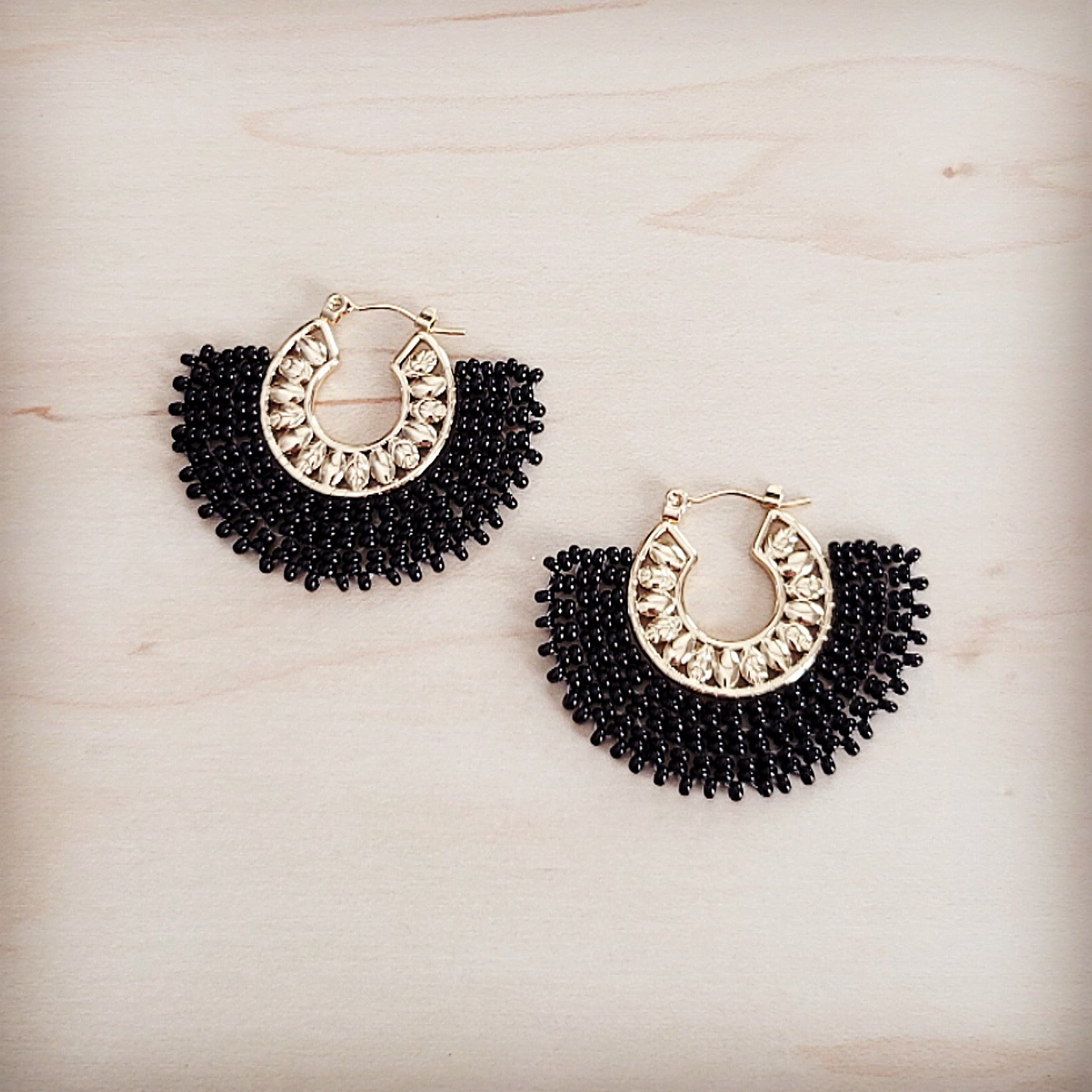 Pair of gold-tone hoop earrings with a semi-circular fan of black seed beads and small clear crystal accents on a light wood background.