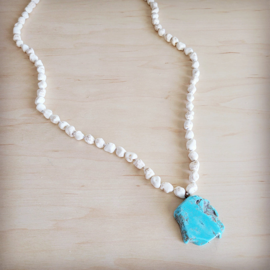 Long white turquoise stone bead necklace with a large natural blue turquoise slab pendant resting on a wooden background