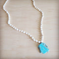 Long white turquoise stone bead necklace with a large natural blue turquoise slab pendant resting on a wooden background