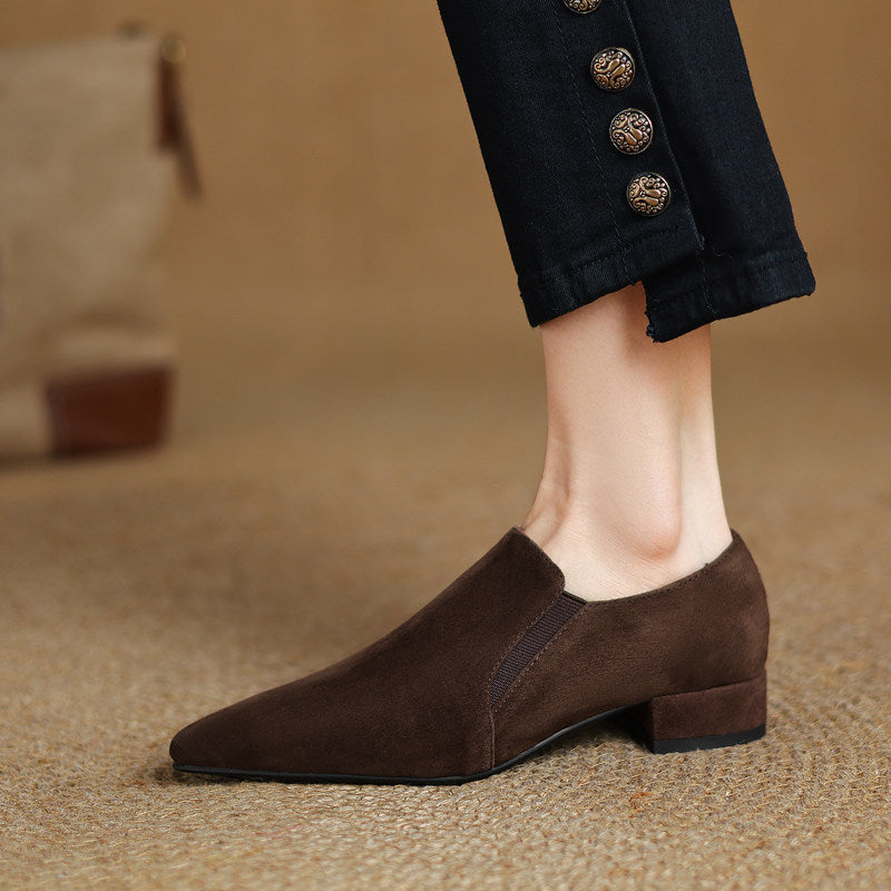 Side view of dark brown suede pointed toe pumps with a low chunky heel, showing the deep vamp cut and elastic detail.
