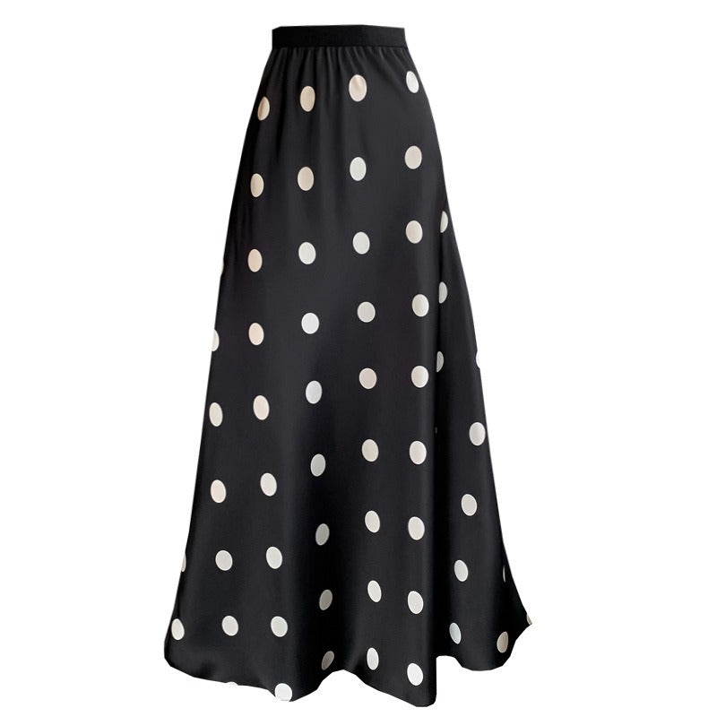 Full-length view of a women's black polka-dot high-waisted A-line maxi skirt with a flowing fishtail hem. Also a lifestyle image of a model wearing a cream polka-dot high-waisted A-line maxi skirt.