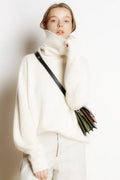Model wearing a thick white ribbed turtleneck cashmere blend sweater with a long-sleeve, relaxed fit.