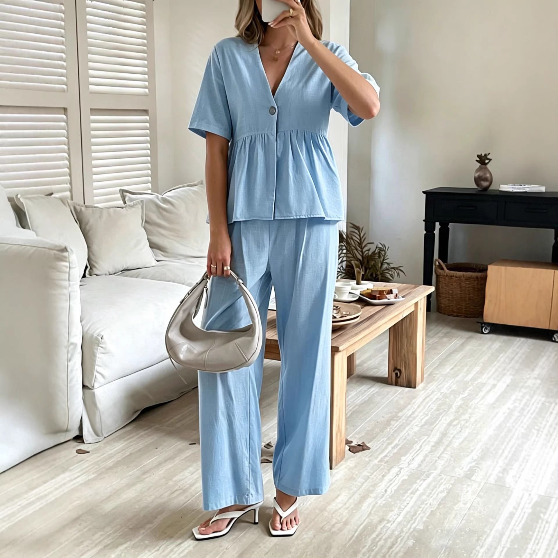 A woman wearing a vibrant orange V-neck peplum top with matching wide-leg pants, styled with a handbag and white sandals.