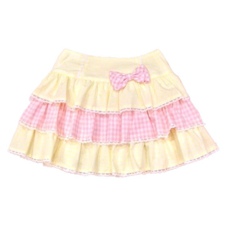 Yellow and pink gingham tiered ruffle mini skirt with a pink bowknot detail, displayed against a light pink polka dot background.