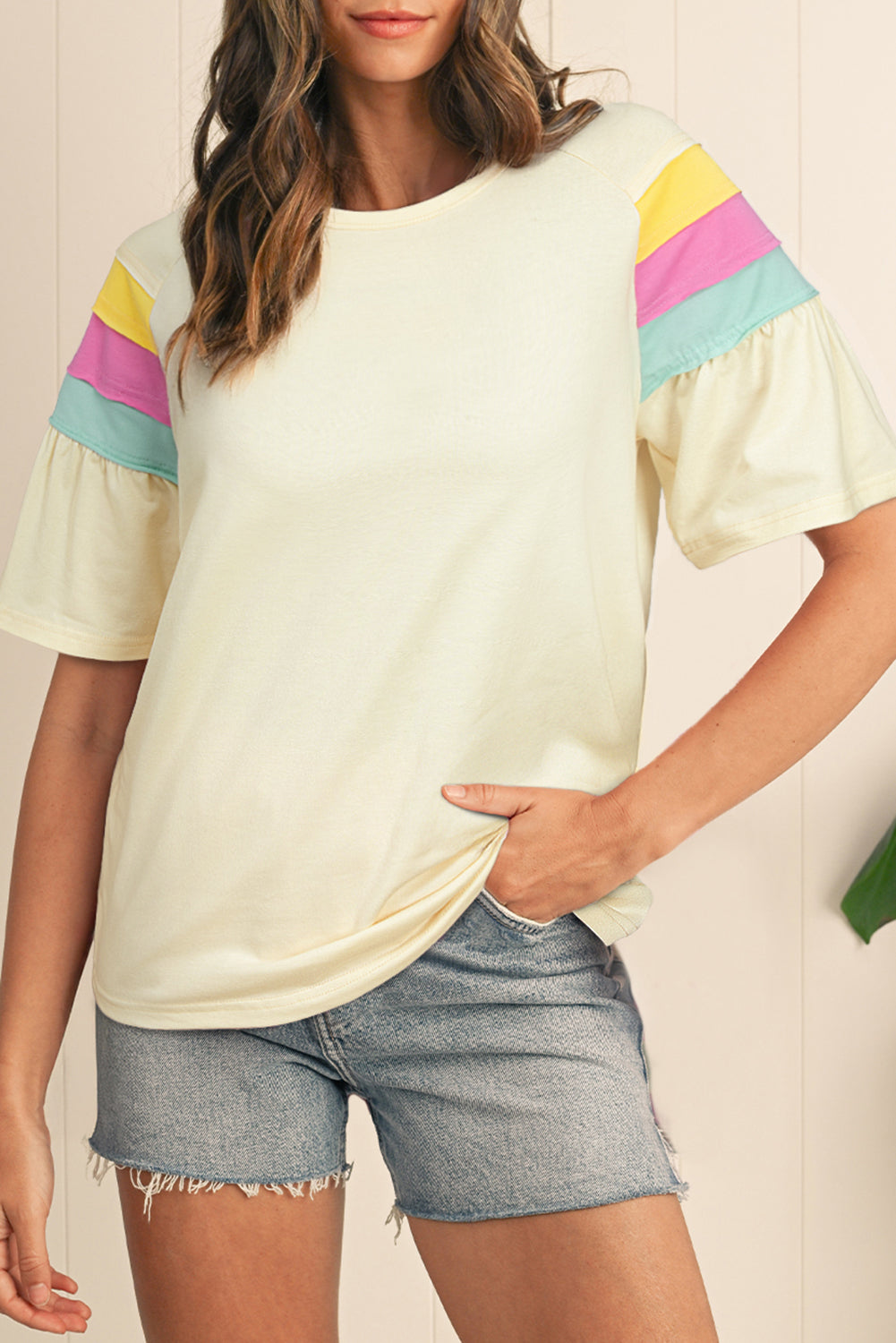 Model wearing a white t-shirt with pastel striped colorblock details on the shoulders and flounce sleeves.