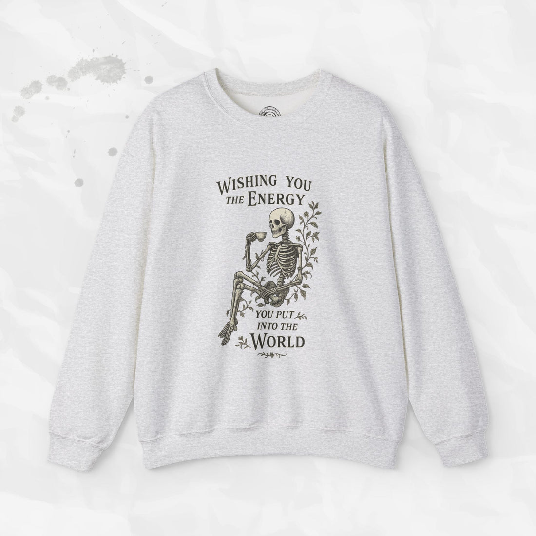 A beige crewneck sweatshirt with a skeleton graphic holding a coffee cup and the text Wishing You the Energy You Put Into the World.