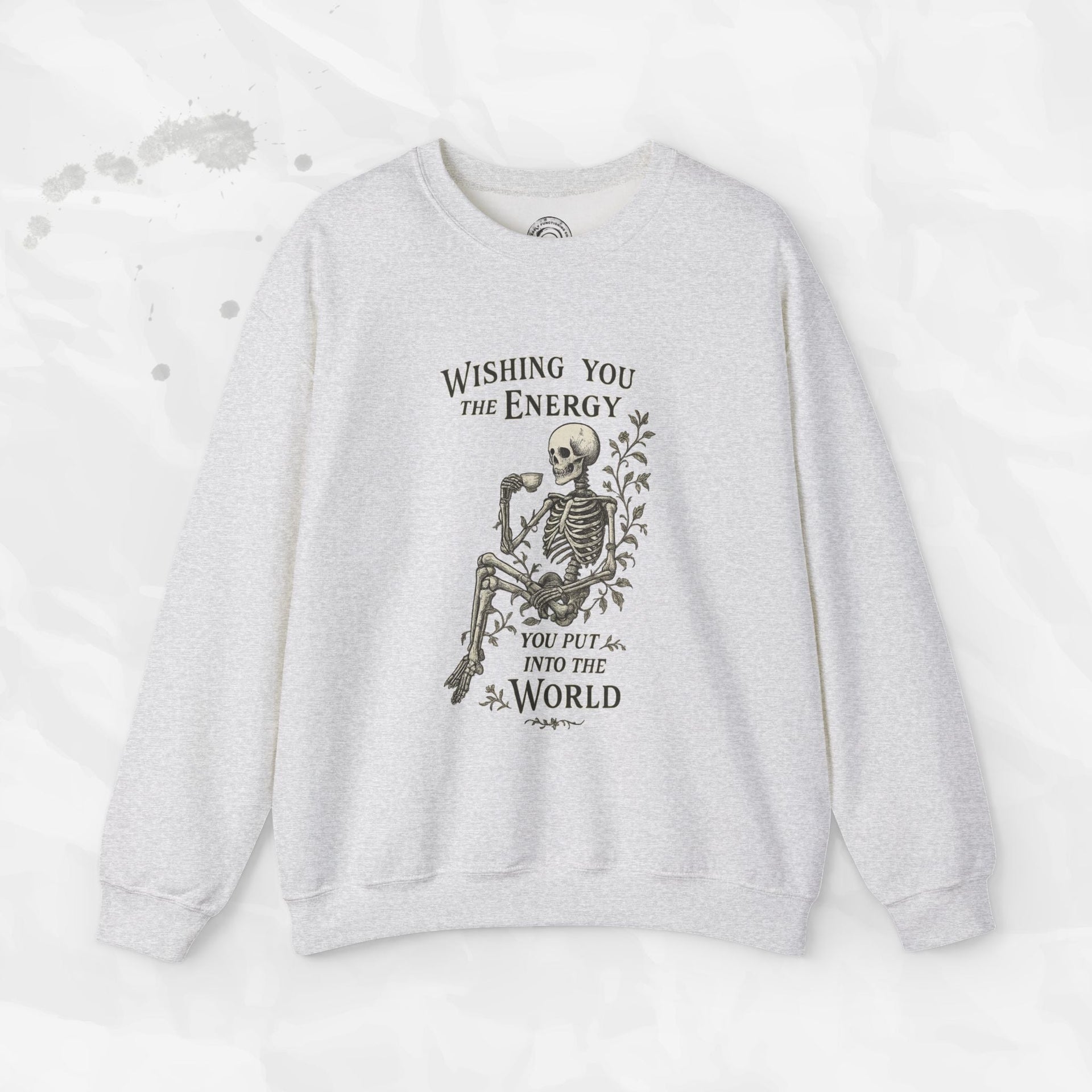 A beige crewneck sweatshirt with a skeleton graphic holding a coffee cup and the text Wishing You the Energy You Put Into the World.
