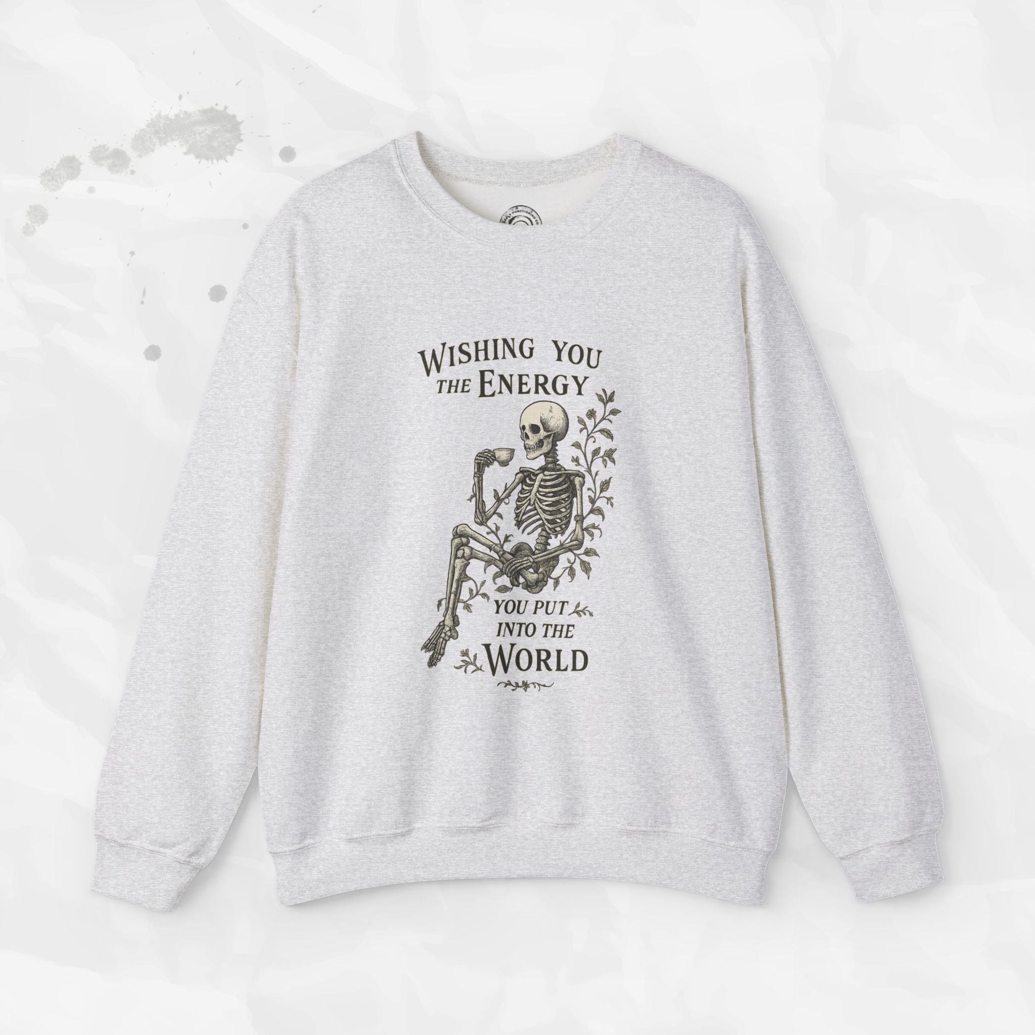 A beige crewneck sweatshirt with a skeleton graphic holding a coffee cup and the text Wishing You the Energy You Put Into the World.