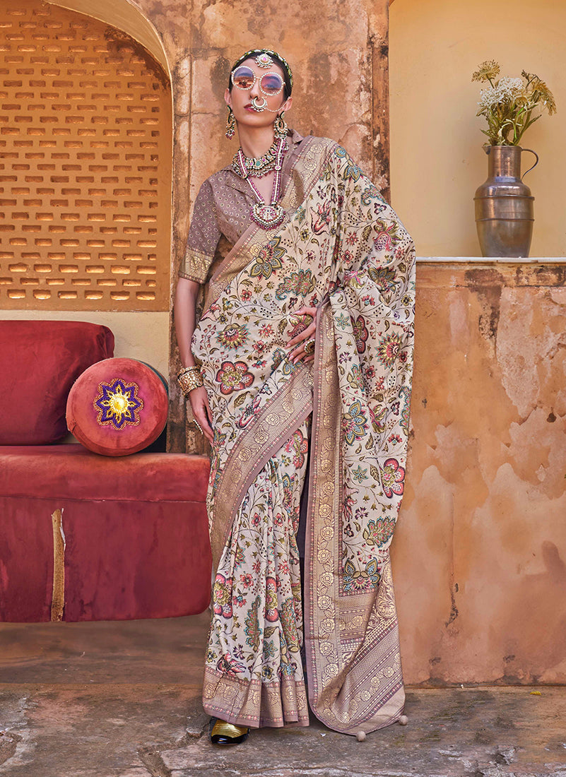 Elegant cream silk blend saree with floral prints, woven border, and decorative tassels.