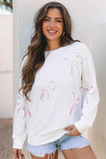 Model wearing a white oversized sweatshirt with pink sequin bow patterns and a crew neckline
