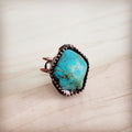 Natural blue turquoise stone set in a dark antique copper ring band on a wooden background