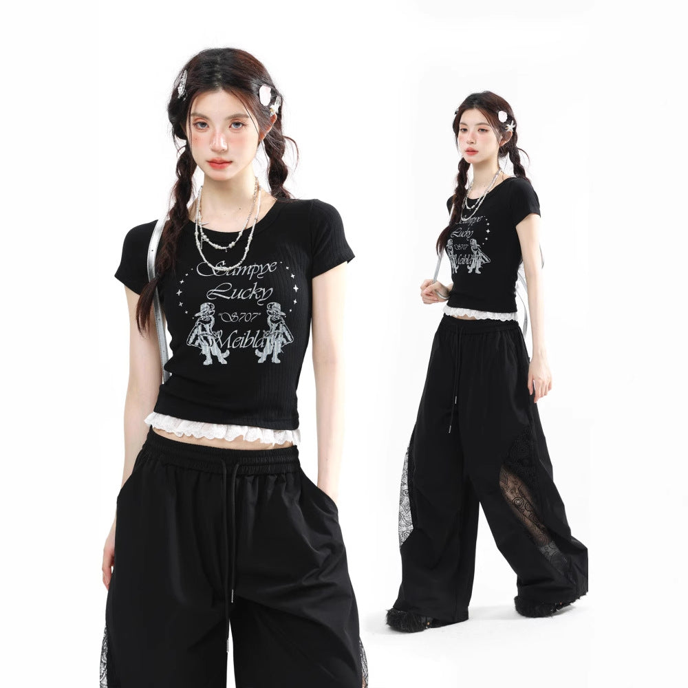 A model wearing a black ribbed short-sleeved t-shirt with a white graphic print and a delicate white lace trim on the hem, paired with black wide-leg pants. The tee features text 'Samppe Lucky 06707 Meiblo' and cartoon figures.