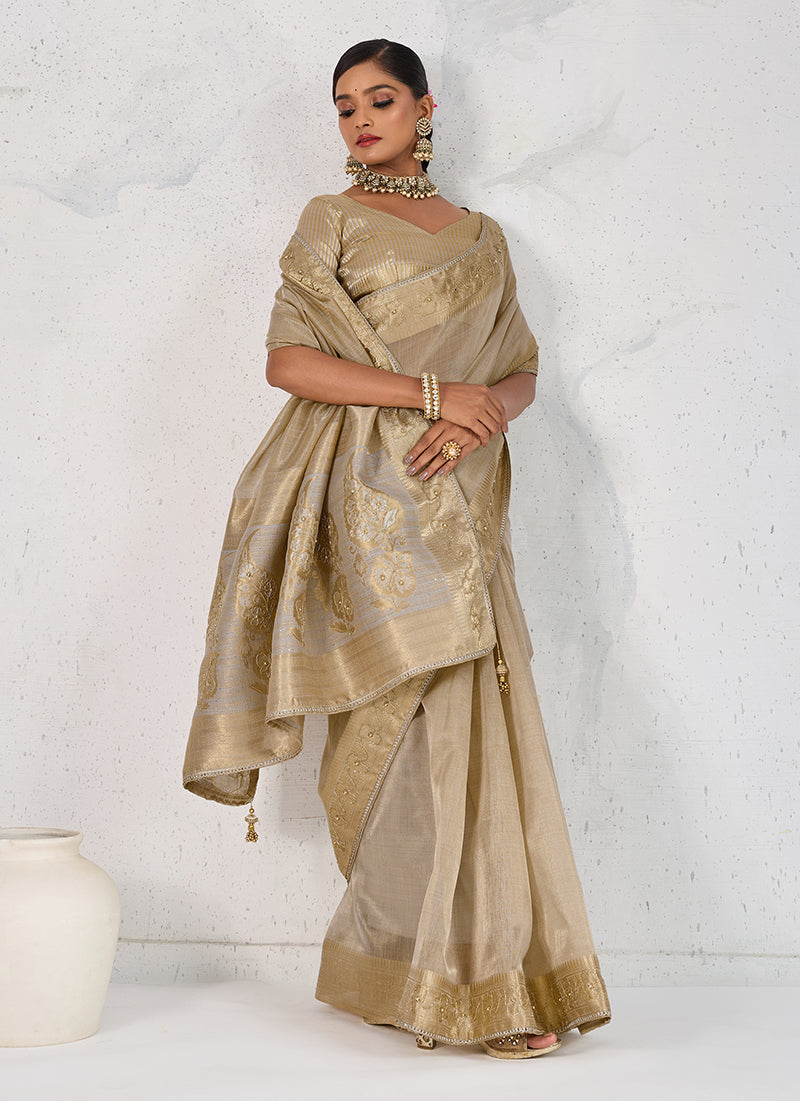 A elegant beige tissue linen saree with intricate woven patterns and hand embroidery, styled for a traditional look.