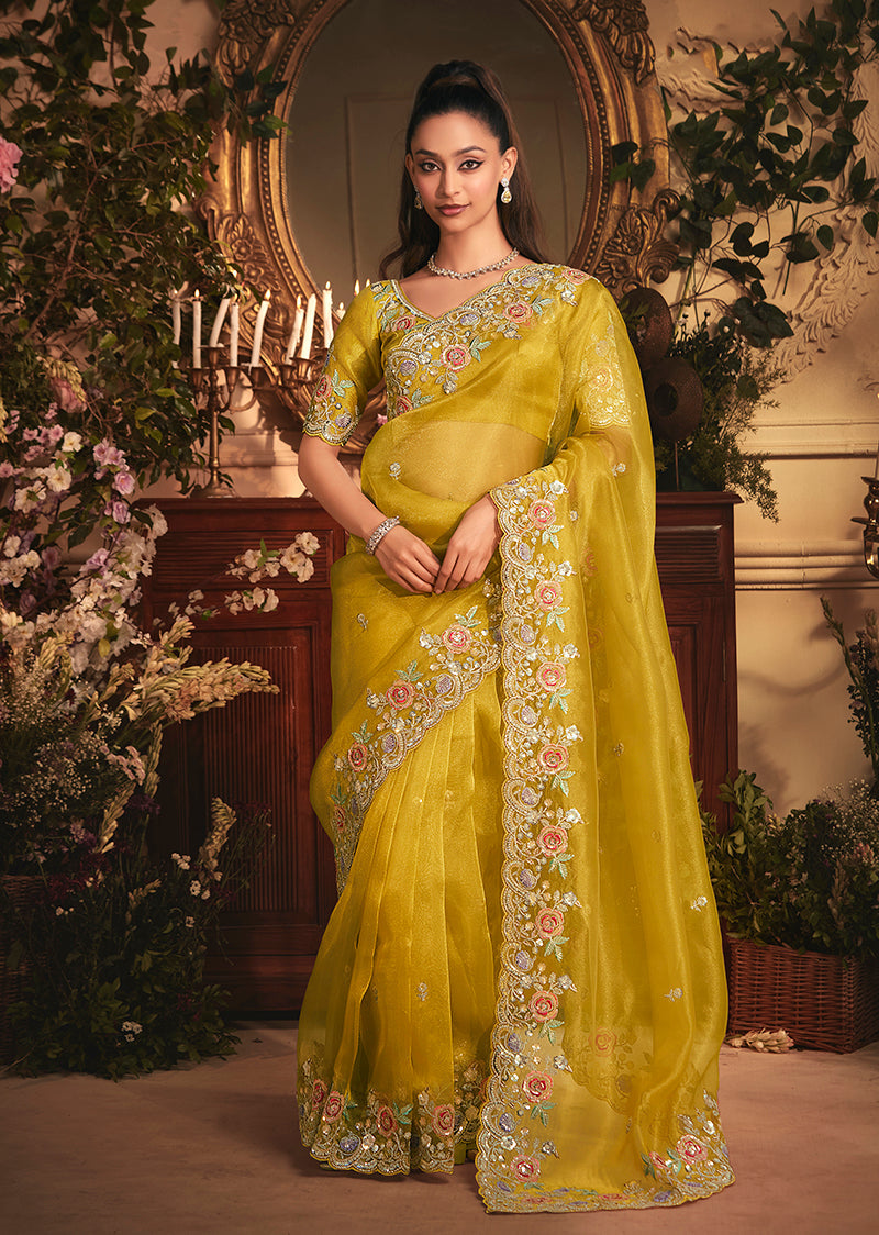 Mustard tissue organza saree with all-over butta work and a heavy stone-embellished border draped elegantly.