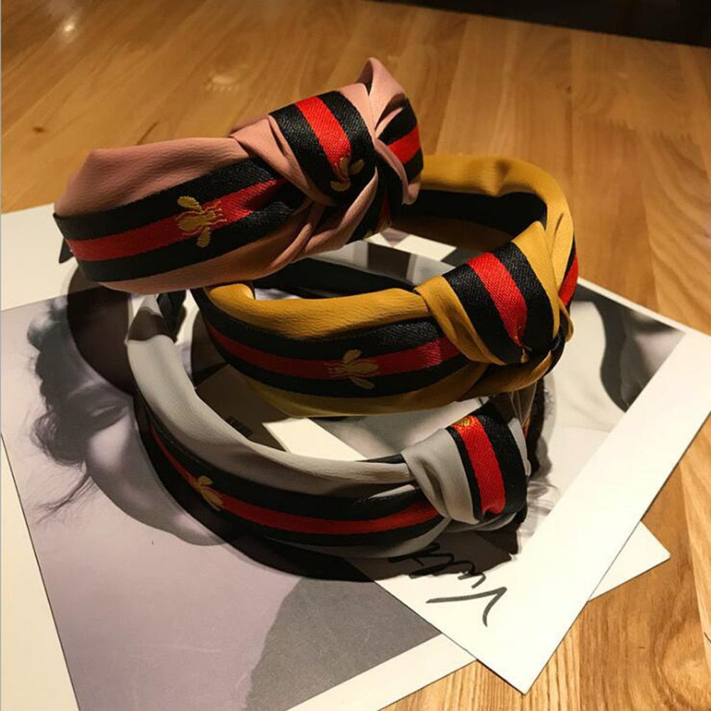 Collection of multi-colored striped bee knot turban headbands for women, including pink, mustard yellow, grey, and navy blue options, featuring a distinctive bee pattern.