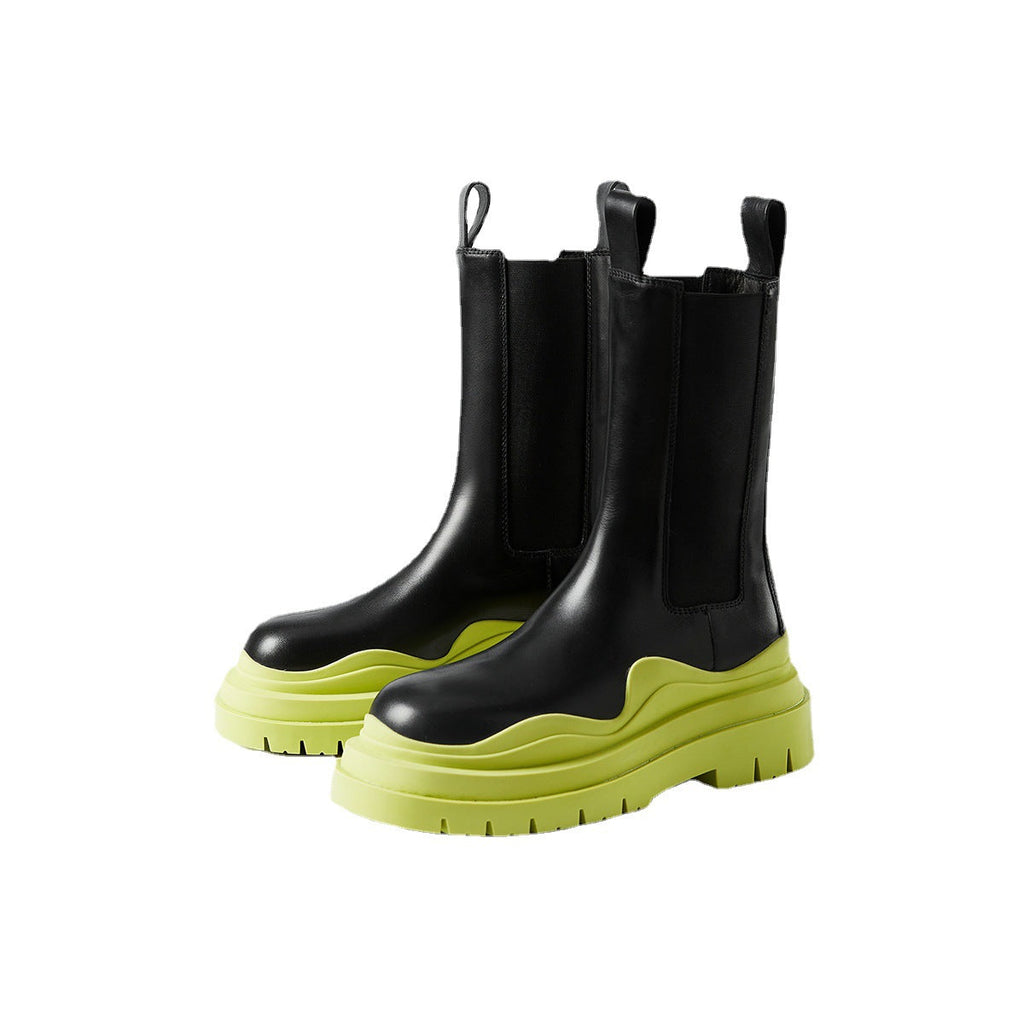 Pair of women's black mid-calf Chelsea boots with a chunky neon green sole on a minimalist background.