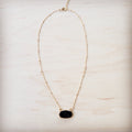 A gold-tone chain necklace with small metal knots and an oval black druzy pendant on a light wood background.