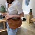 A stylish half-round women's shoulder bag made of soft PU leather with a decorative wide belt and metal chain detail.