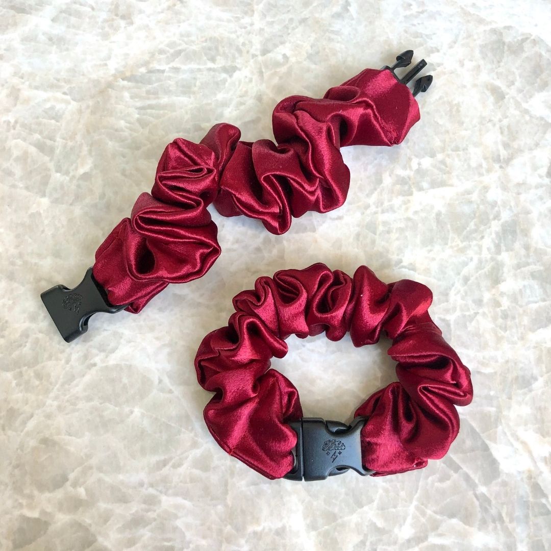 A cherry red hair scrunchie with an adjustable buckle closure for easy, snag-free removal.