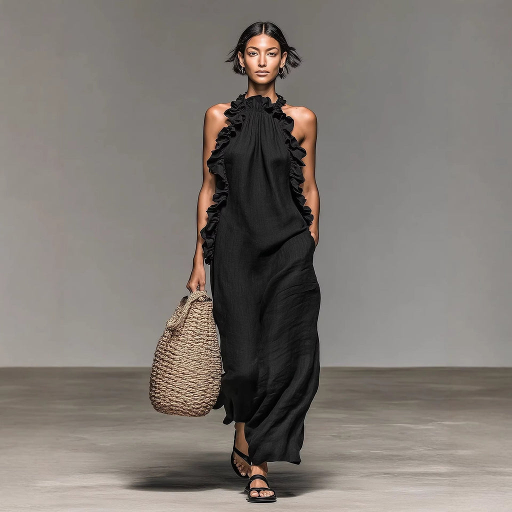 A woman wearing a black sleeveless ruffled halterneck maxi dress with an open back, walking on a city street.