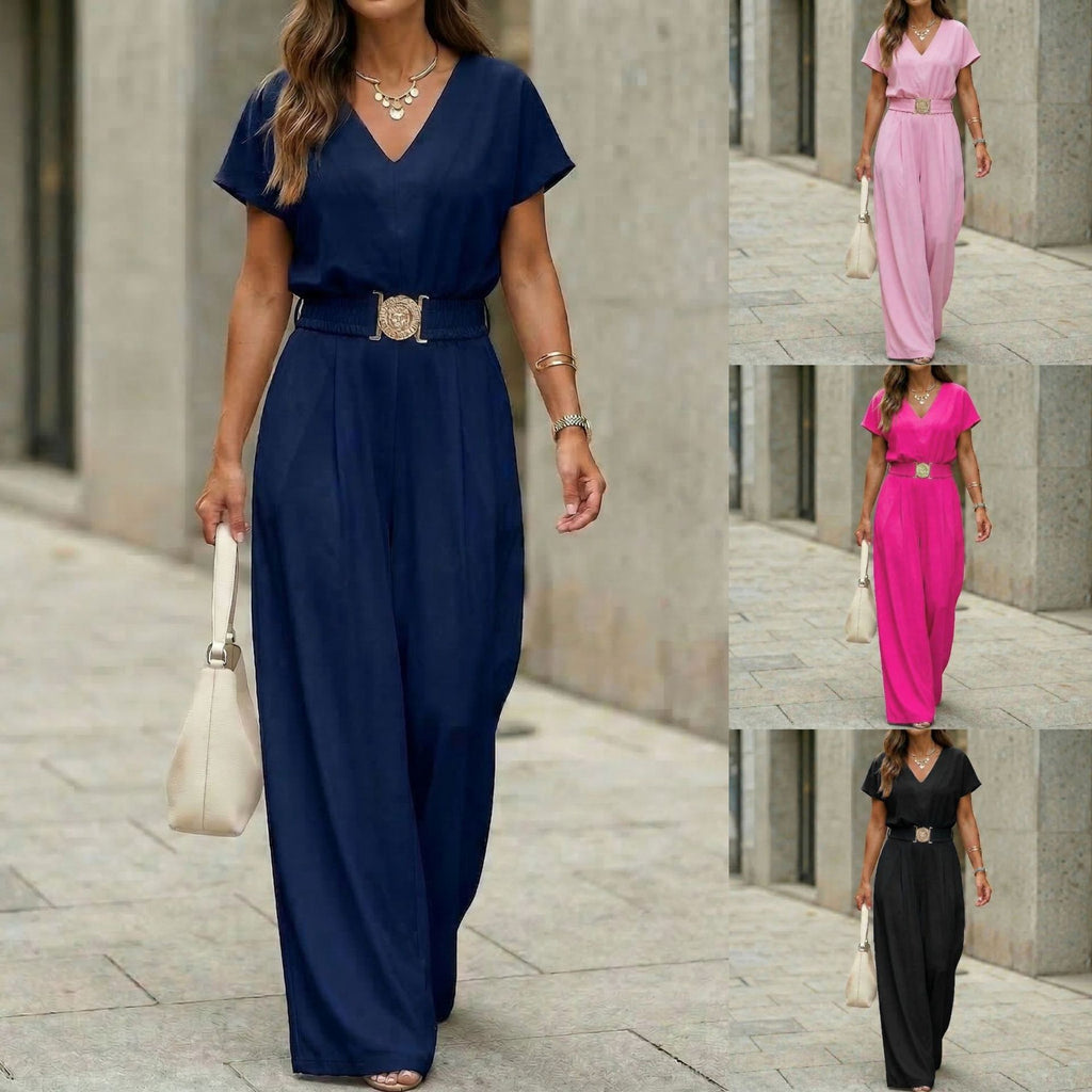 A woman wearing a navy blue V-neck wide-leg jumpsuit with a gold-buckle belt, paired with a white handbag in a city setting.