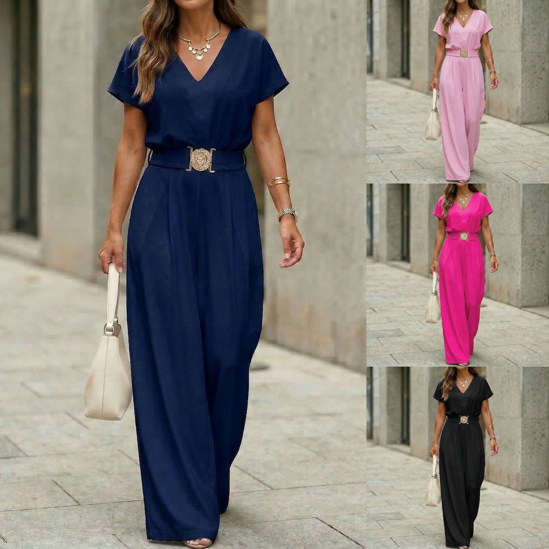 A woman wearing a navy blue V-neck wide-leg jumpsuit with a gold-buckle belt, paired with a white handbag in a city setting.