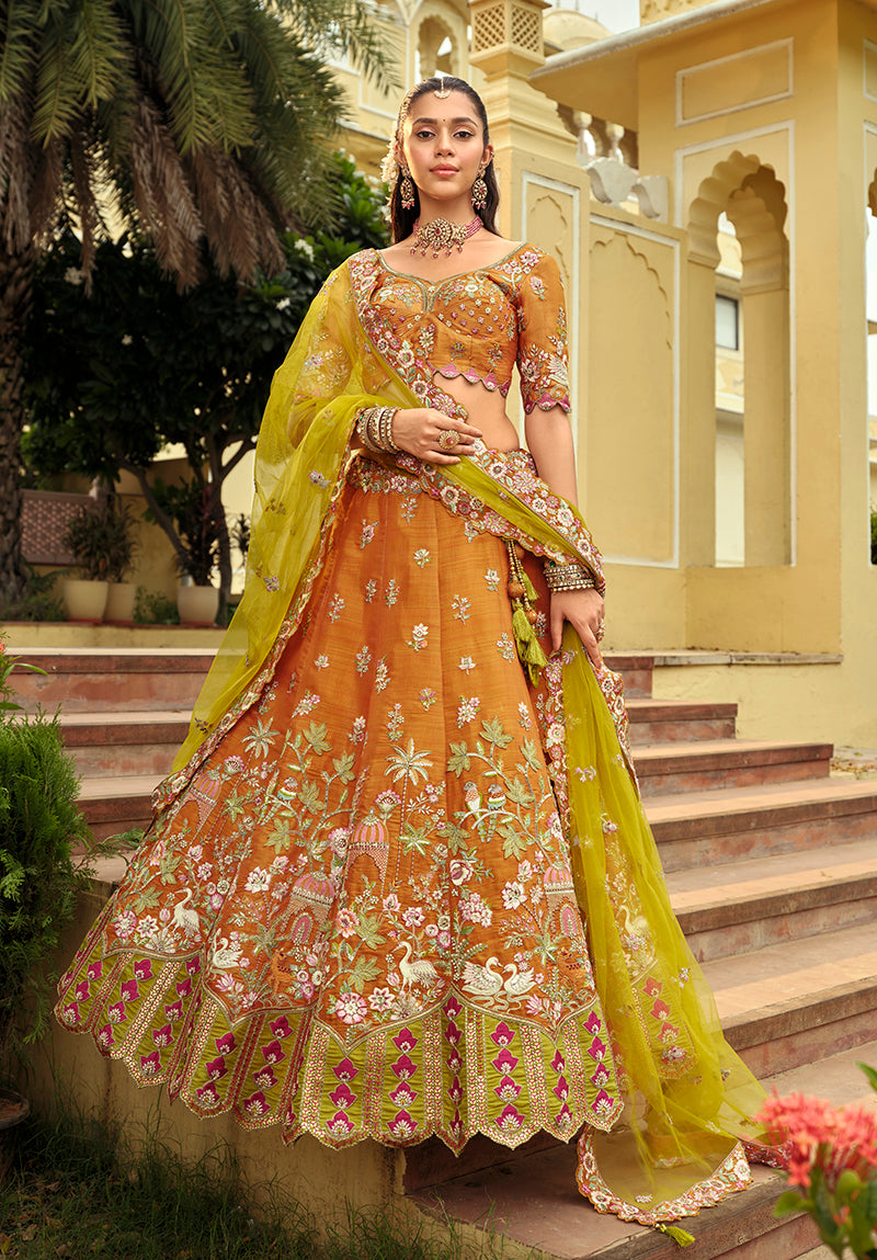 Close up of an amber and lime-green silk lehenga choli featuring heavy decorative embroidery.