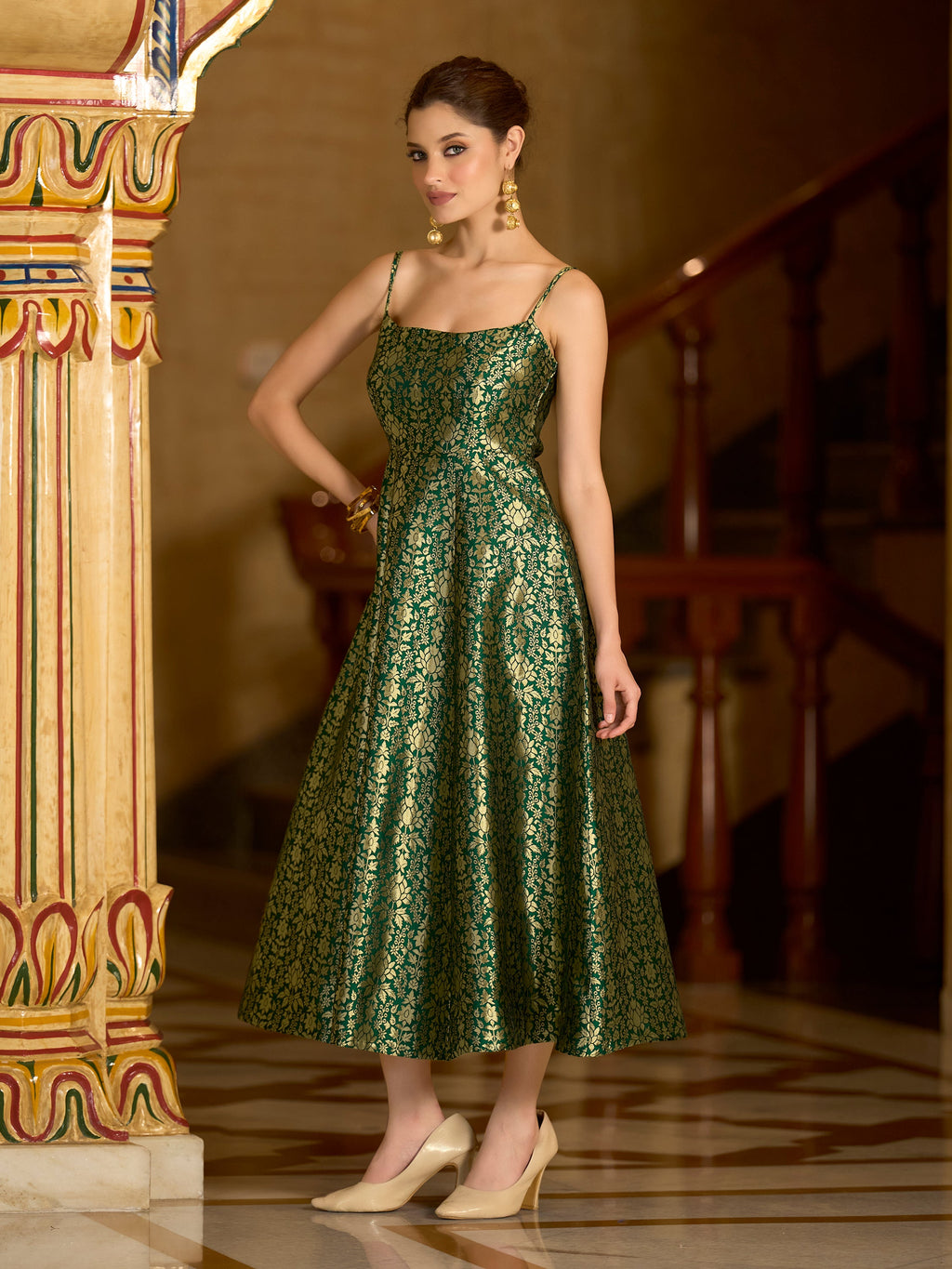 Woman wearing a green jacquard A-line dress with intricate gold zari weaving, square neckline, and strappy shoulders.