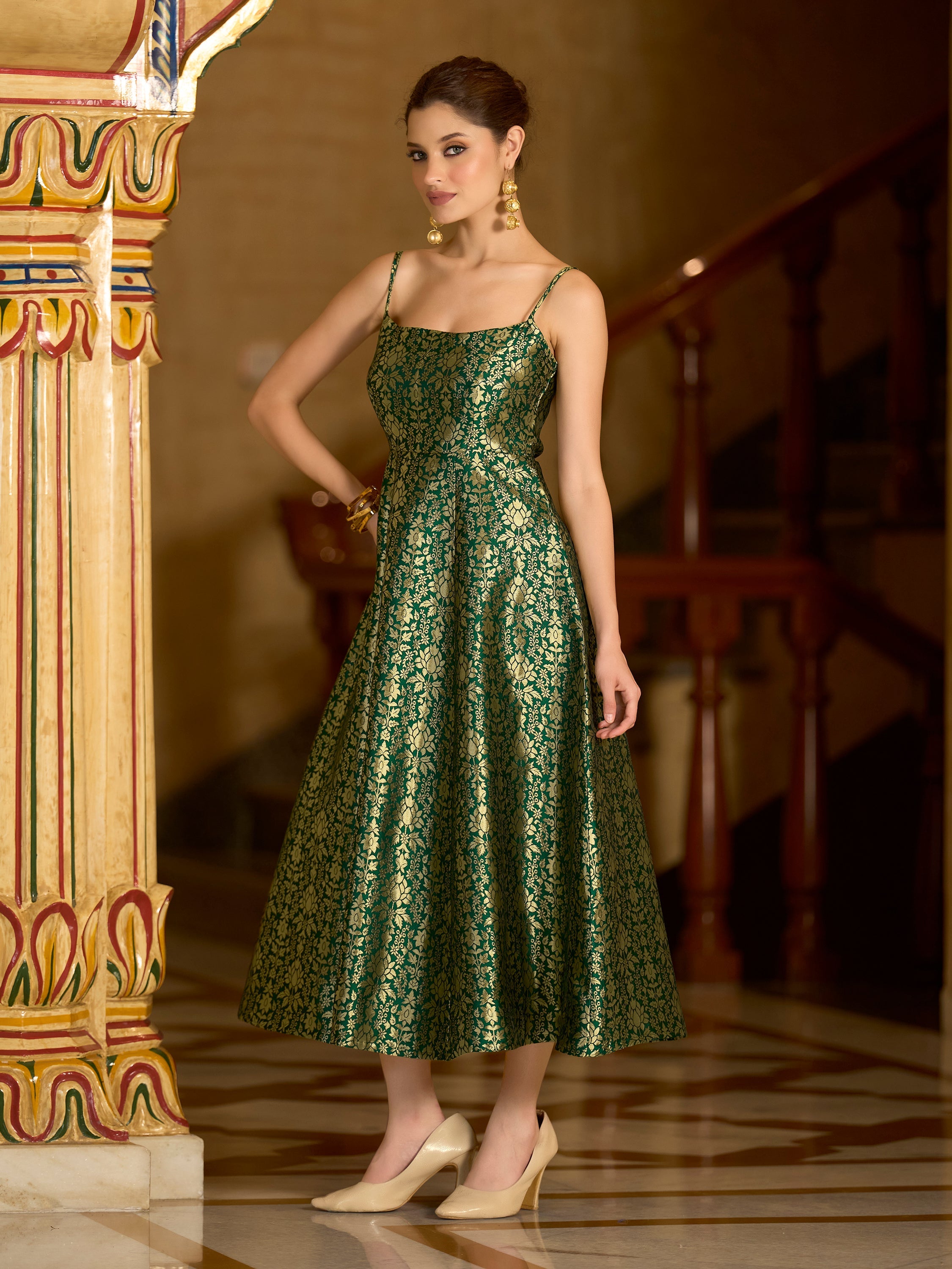 Woman wearing a green jacquard A-line dress with intricate gold zari weaving, square neckline, and strappy shoulders.