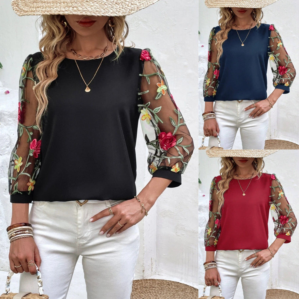 A woman wearing a solid color top with sheer mesh sleeves featuring floral embroidery.
