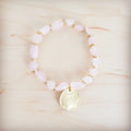 Rose quartz beaded stretch bracelet with a gold-tone coin charm on a light wooden background.