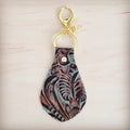 Embossed leather key chain with a turquoise and brown floral pattern and gold-tone metal hardware on a light wood background.