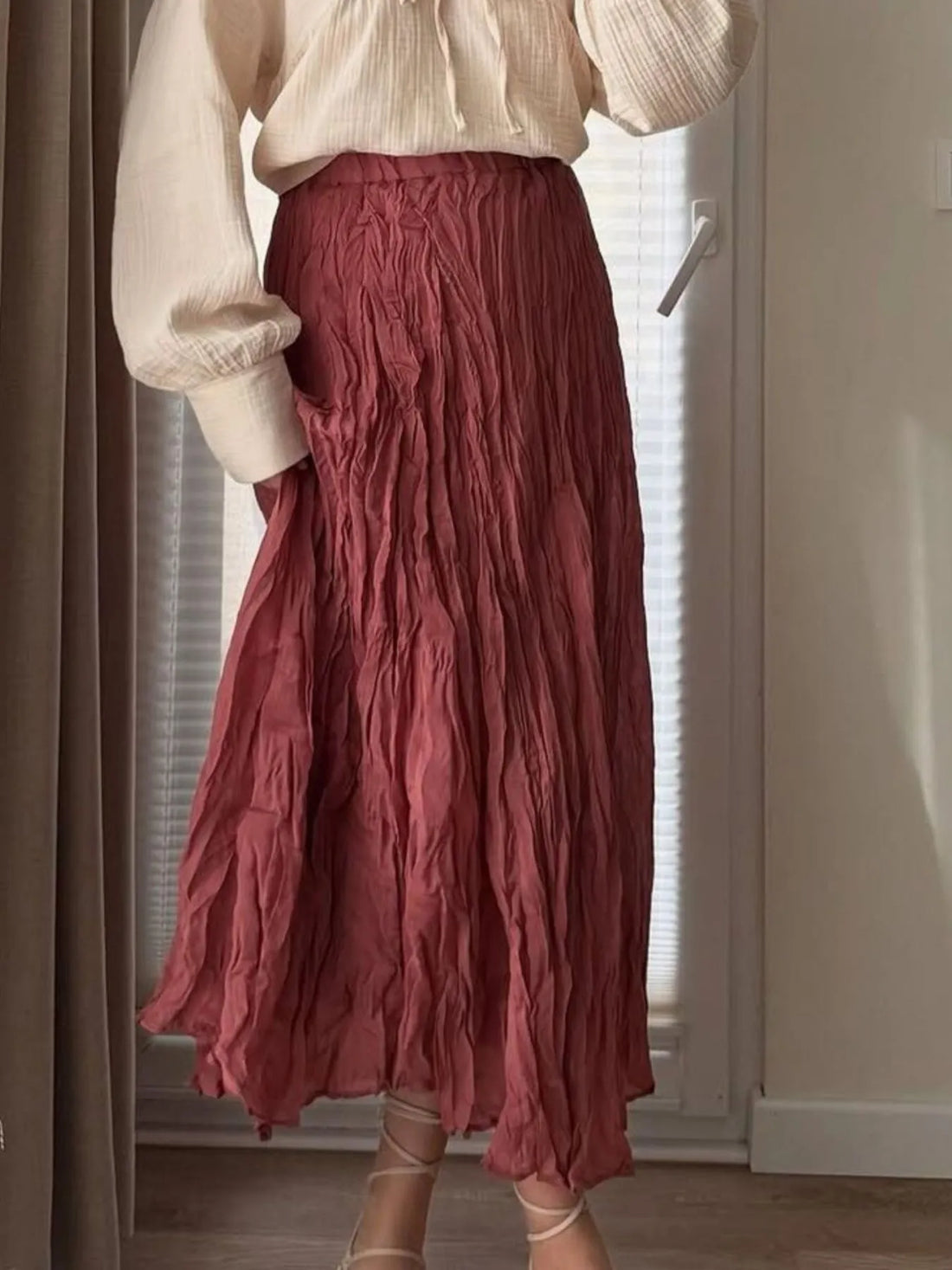Model wearing a dusty rose ruched elastic waist midi skirt paired with a beige top and strappy heels