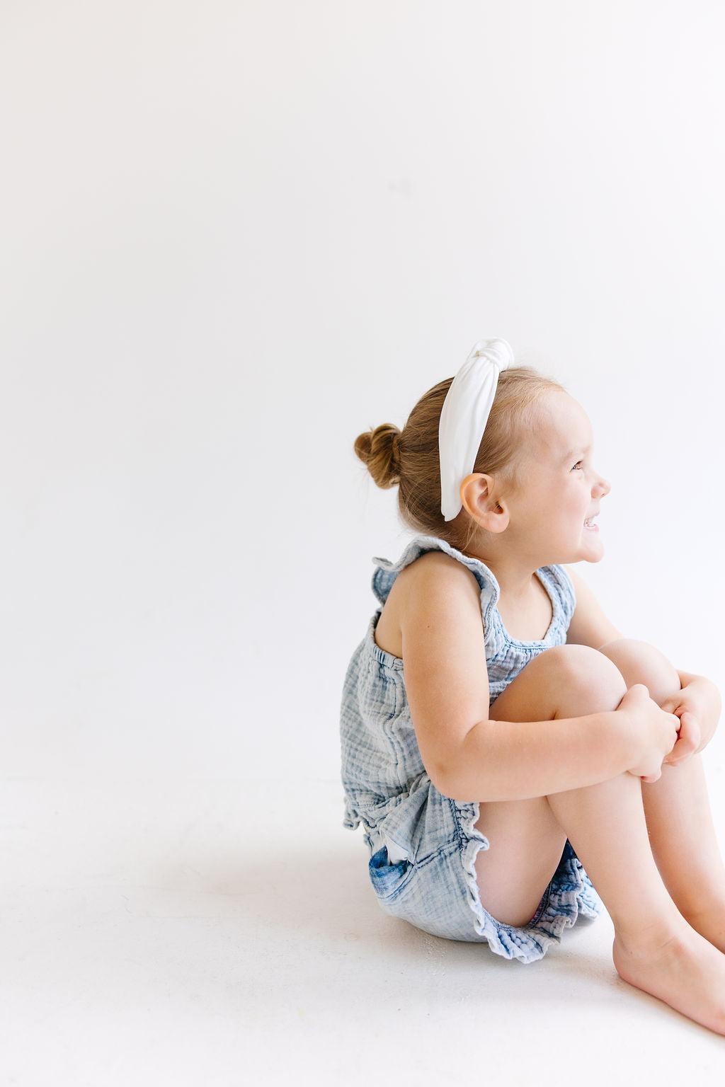 A young girl wearing a solid white fabric knotted headband, side view