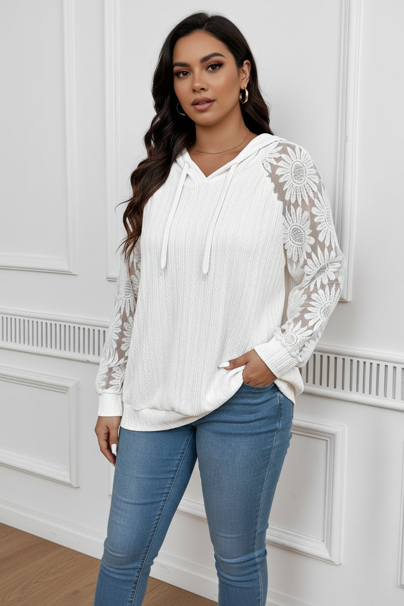 A woman wearing a white long-sleeve hoodie featuring floral hollow-out lace sleeves and a textured knit bodice.