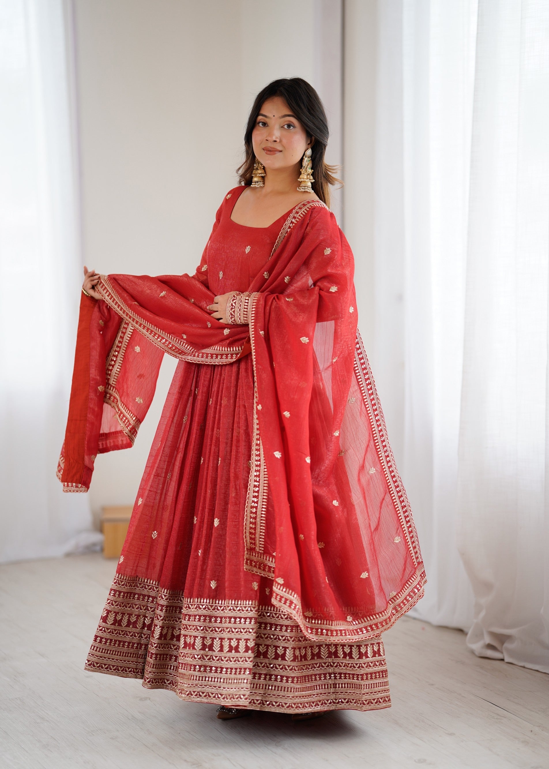 Woman wearing a rust-colored silk Anarkali gown with gold Jari and sequence embroidery work and matching dupatta