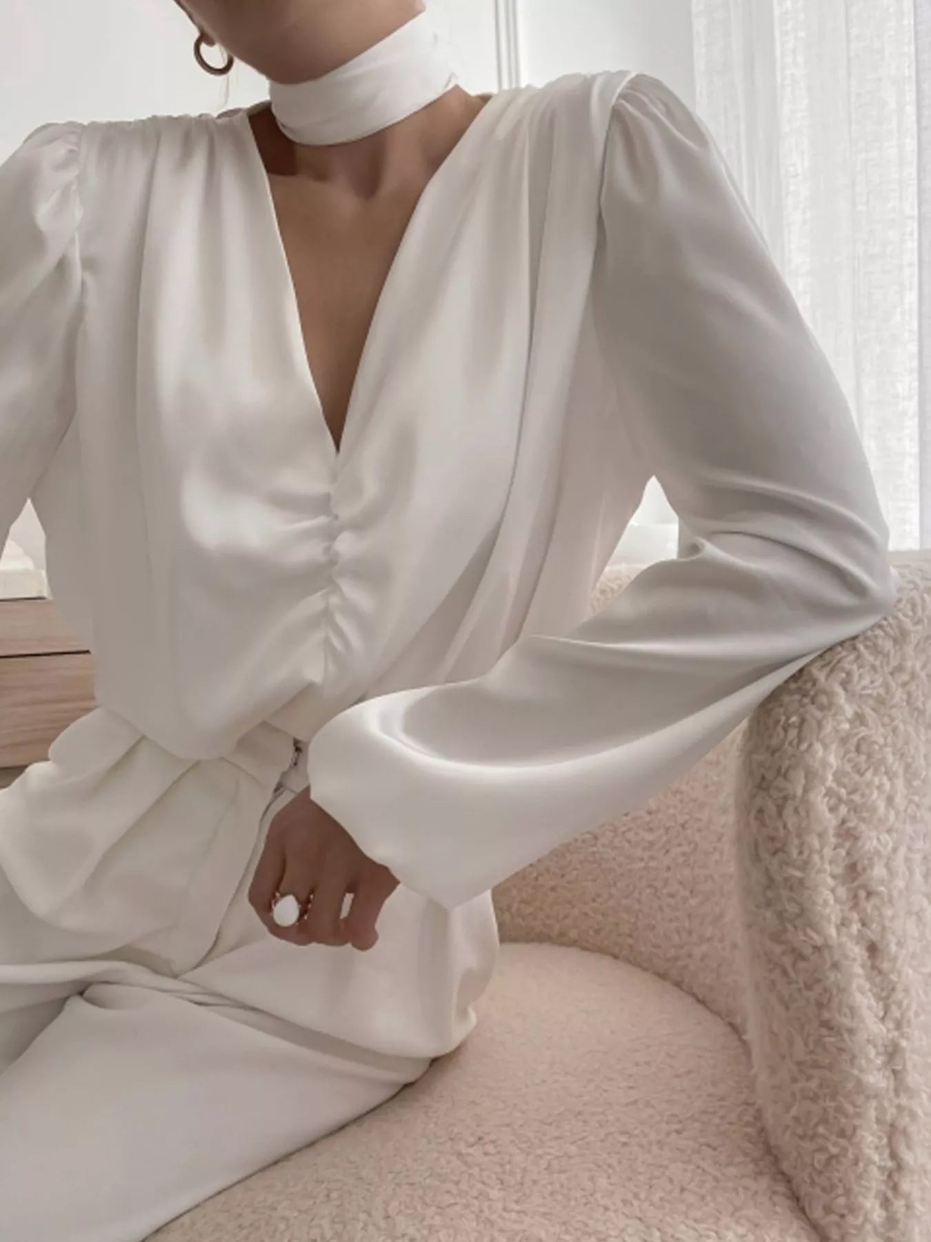 A woman wearing a white long-sleeve blouse with a deep V-neck and ruched detailing at the front.