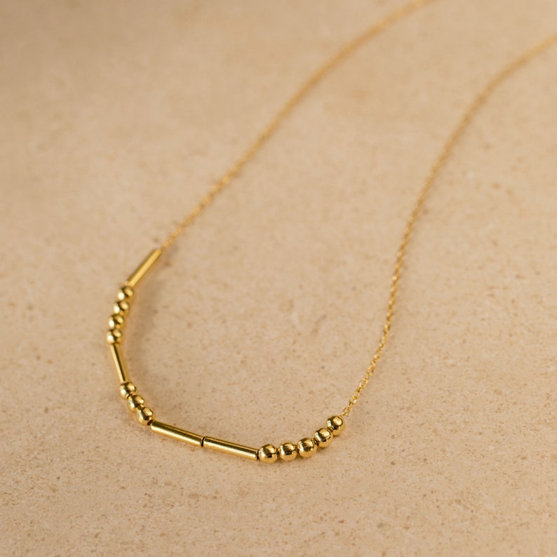 Elegant, minimalist Morse Code custom name pendant necklace displayed on a neutral background.