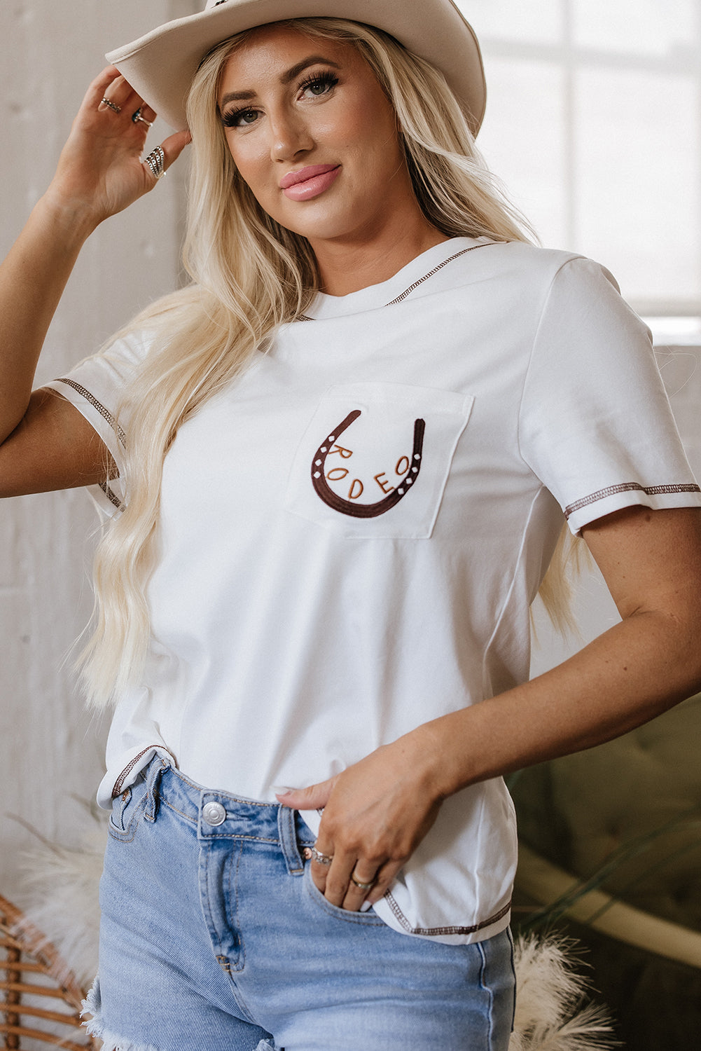 Front and back view of a white t-shirt with a horseshoe embroidered patch pocket and contrast stitching.