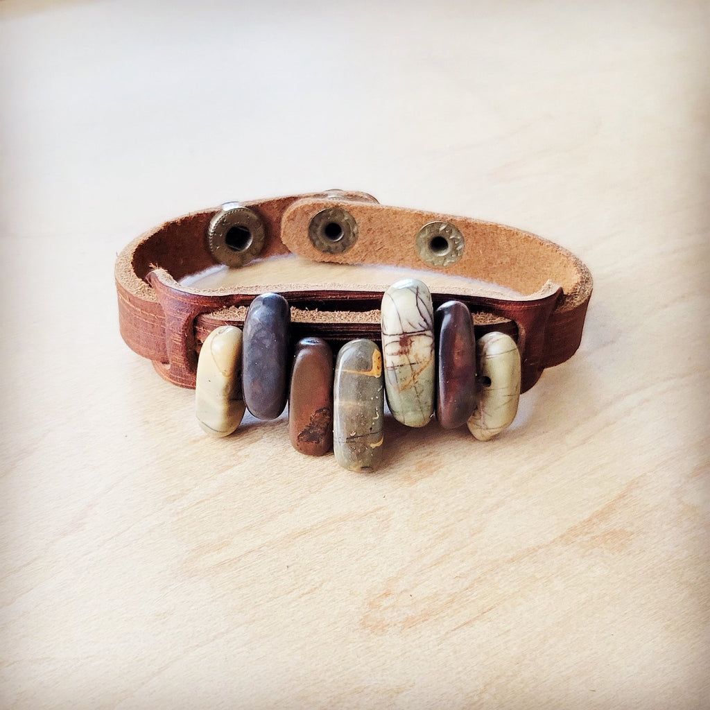 Close up of a handcrafted genuine leather cuff bracelet adorned with varied natural Picasso Jasper stone beads and a double snap closure.