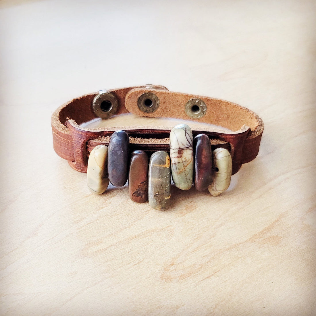 Close up of a handcrafted genuine leather cuff bracelet adorned with varied natural Picasso Jasper stone beads and a double snap closure.