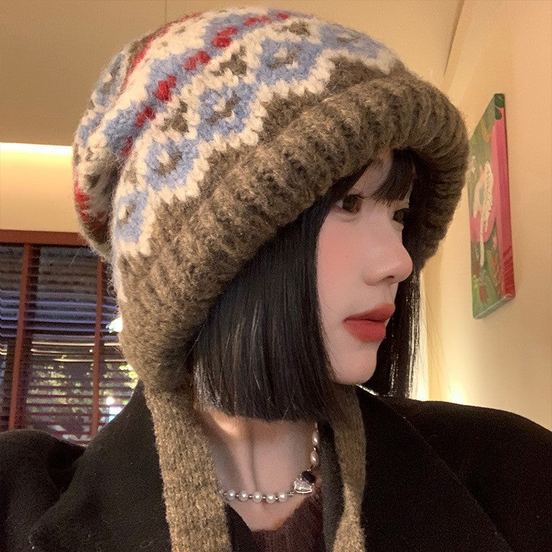 A person wearing a vintage-style wool winter earflap hat with a blue, red, and brown Nordic geometric pattern.