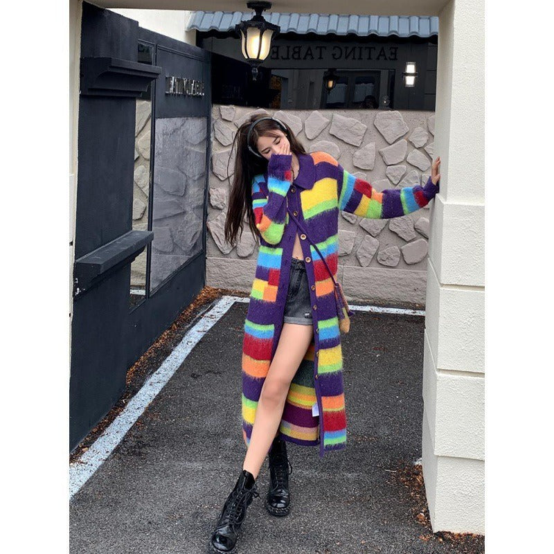 Woman wearing a long rainbow striped knit cardigan with a V-neck collar and button closure, styled with black shorts and boots.
